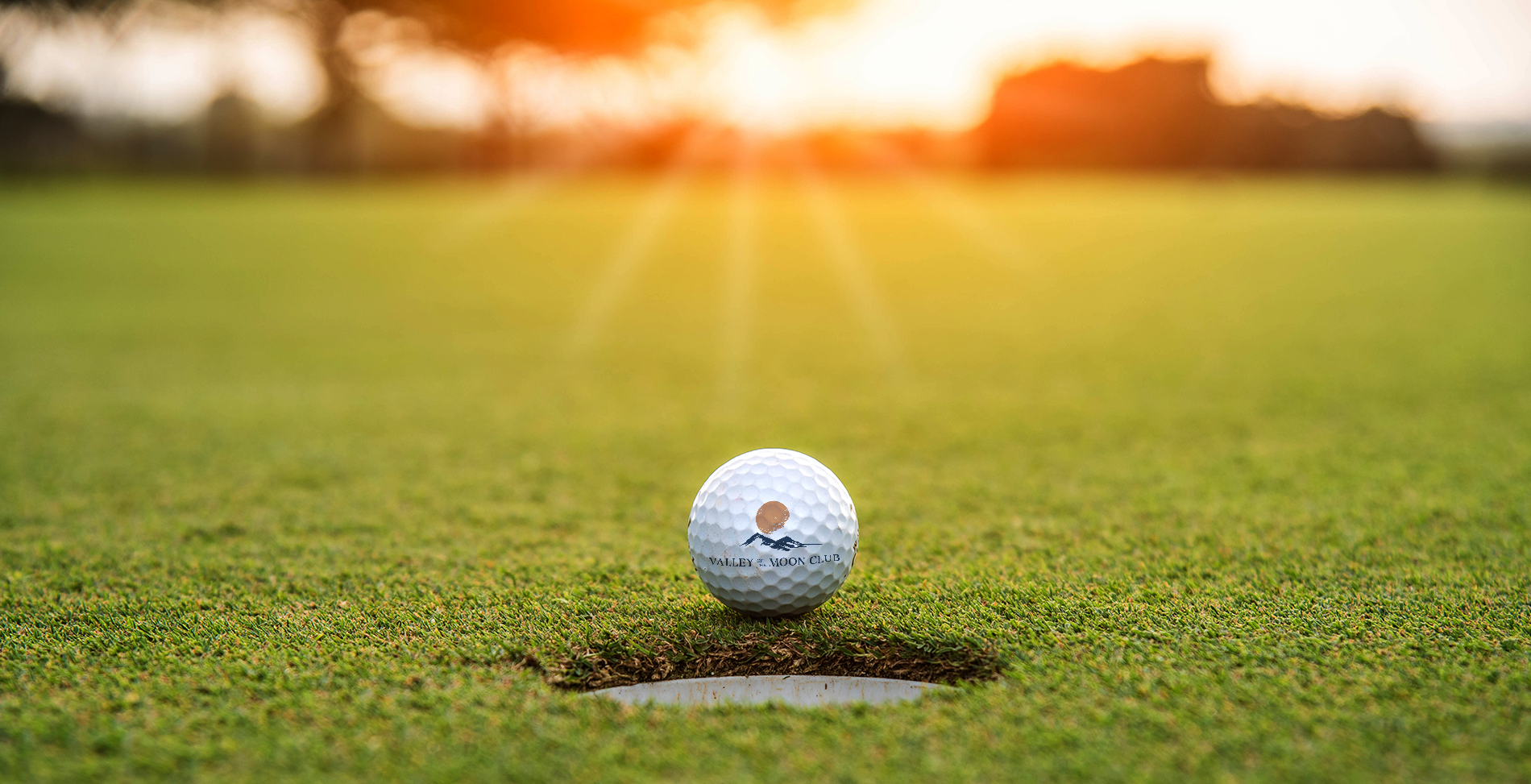 Image of golf ball at edge of hole with sun set in background